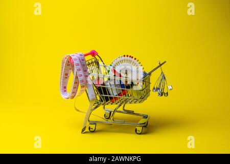 sewing accessories in the grocery basket, needles, threads, scissors, thimble on a yellow background Stock Photo