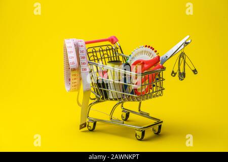 sewing accessories in the grocery basket, needles, threads, scissors, thimble on a yellow background Stock Photo