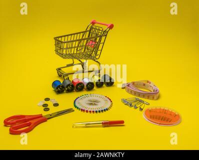 Spools of thread and basic sewing tools including pins, needle, a thimble, and tape measure. Copy space. Long banner format On a yellow background Stock Photo