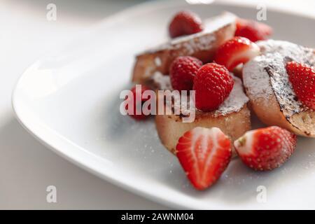 French toast with strawberries and raspberries, sprinkled with powdered sugar. Dessert on a white plate Stock Photo