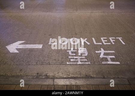Arrow and 'look left' caution or sign written in English and Chinese on a street in Hong Kong, China. Stock Photo