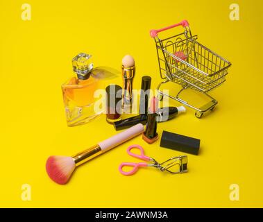 Makeup products fondant, mascara, perfume, brush, with cosmetic bag shopping cart on yellow background c Stock Photo