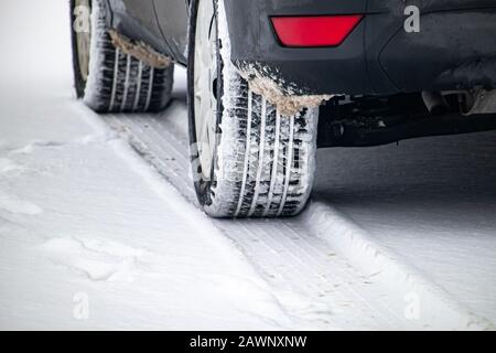 The tires of an automobile are caked in snow as the vehicle is stopped in a parking lot. The fresh snowfall has left snow embedded in the treads. Stock Photo