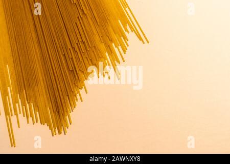 Thin, long, uncooked and dry spaghettini noodles are spread out on a flat white surface, with the noodles entering the frame above and leaving open ne Stock Photo