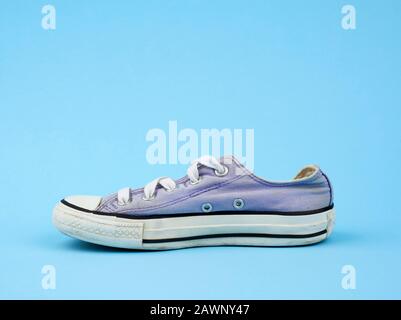 purple worn textile sneaker with white laces on a light blue background, side view of shoes Stock Photo