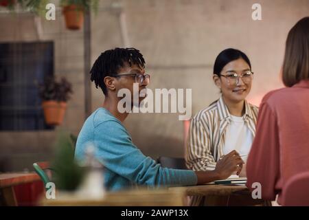 Multi-ethnic group of three young people working on project together while sitting at table in cafe, copy space Stock Photo