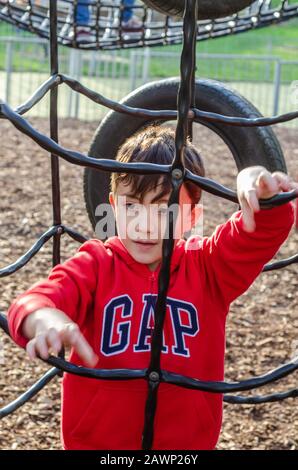 A young boy happy playing on a climbing frame in a children's playground. Stock Photo