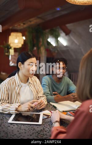 Multi-ethnic group of three business people working on project while sitting at table in cafe against red wall, copy space Stock Photo