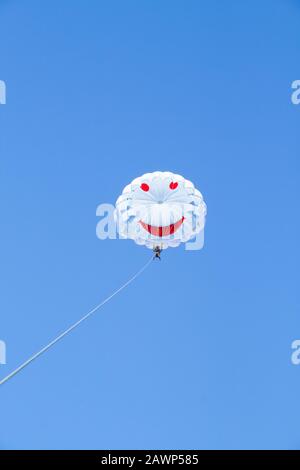 Two people are flying on a white parachute towed by the rope against the blue sky. Parasailing. Sea summer recreation. Stock Photo