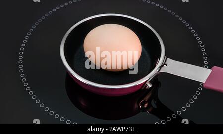 One egg in a tiny little pan, in the middle of the cooking surface. Stock Photo