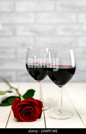 Valentine's Day concept. Two glasses of wine and red rose on a white wooden table. Selective focus. Stock Photo