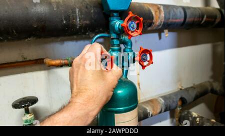 Plumber turning a gate valve on a dosing pot in a dirty old boiler room Stock Photo