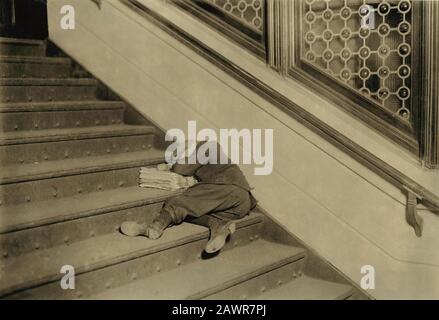 1912 , november , Jersey City, New Jersey, USA  : Newsboy asleep on stairs with papers - NEWSBOYS  , Photos by LEWIS HINE ( 1874 - 1940 ) -  - NEWSBOY Stock Photo