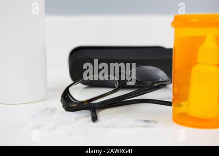 Glasses sitting beside prescription vial, glasses case, eye dropper, and solution bottle. White bathroom counter Stock Photo