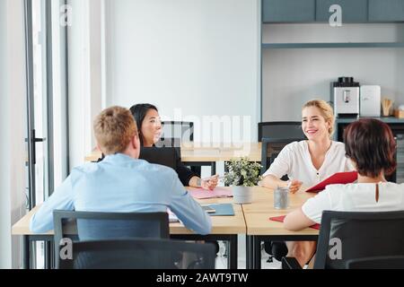 Group of young business executives sitting at big office table and talking about development of new start-up project Stock Photo