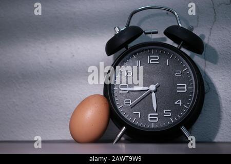 Close up of alarm clock and egg on table at night  Stock Photo