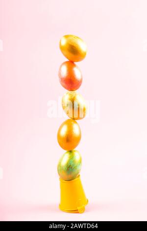 Painted Easter eggs are arranged in a vertical tower and balance on a pink background. Creative easter concept. Stock Photo