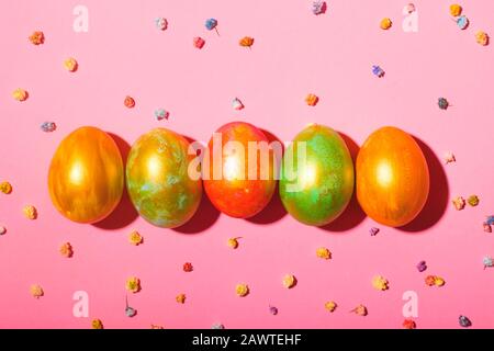 Five colored Easter eggs lie on a pink background among the gypsophila flowers in hard light. Stock Photo
