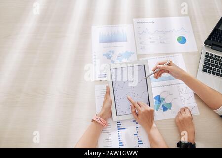 Coworkers sitting at big office table and analyzing chart on digital tablet, view from above Stock Photo