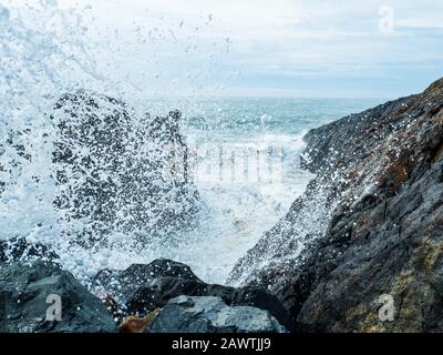 Frothy Foamy sea spray splashes up into the air, almost onto the lens as waves crash into rocks at the break wall, exploding water everywhere Stock Photo