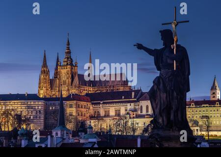 Prague, Czech Republic - Illuminated St.Vitus Cathedral at dusk with clear blue sky taken from Charles Bridge on a winter night. Out of focus statue i Stock Photo