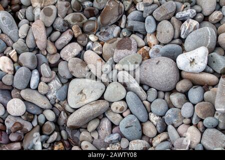 sea pebbles colored granite on the beach background stones. The shore of the beach with sand and pebbles washed by the waves of the sea. Stock Photo
