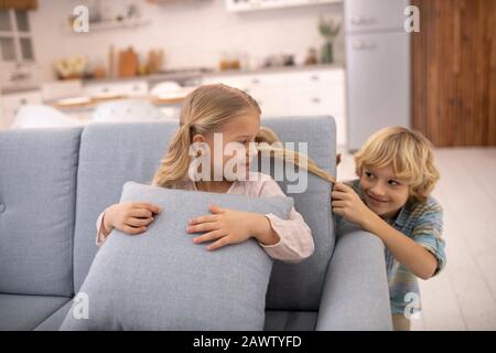 Boy pulling girls ponytail from behind, teasing and feeling joyful Stock Photo