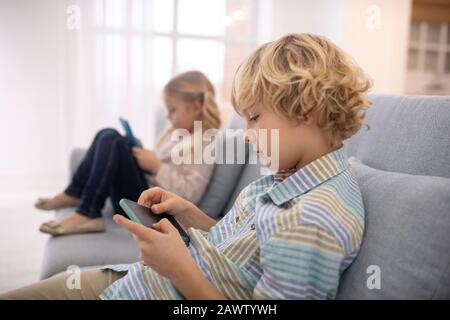 Boy and girl sitting on sofa and playing with gadgets Stock Photo