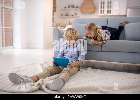 Boy sitting on the floor, girl lying on sofa Stock Photo