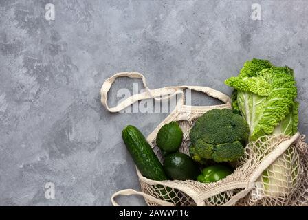Green fresh vegetables in a string bag on a gray concrete background. Flat lay with copy space. Stock Photo