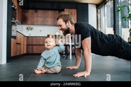Happy father doing push upps next to his infant baby, moved and amused by him. Stock Photo