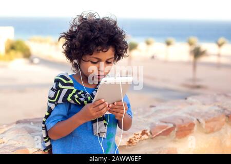 Kid boy playing games on tablet outdoor. Children, technology and gadget addiction concept Stock Photo