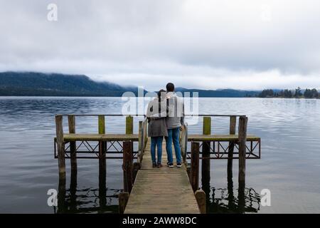 Young Asian couple hugging leaning on shoulder on the bridge Lake Te Anau New Zealand Stock Photo