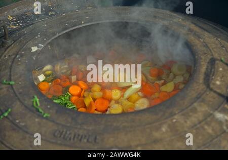 Medieval style cooking of various vegetables in big metal pot Stock Photo