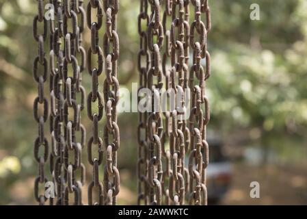 Vertical hanging rusty iron chains showing weathering covered with cobwebs. Stock Photo