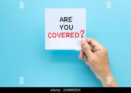 hand holding paper with question ARE YOU COVERED? isolated on blue background with copy space. travel insurance concept Stock Photo