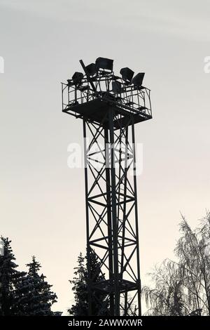Black silhouette of metal construction with spotlights on top. Dark silhouettes of trees on background of light bright sky. Stock photo with empty space for text for web, print, wallpaper, background Stock Photo