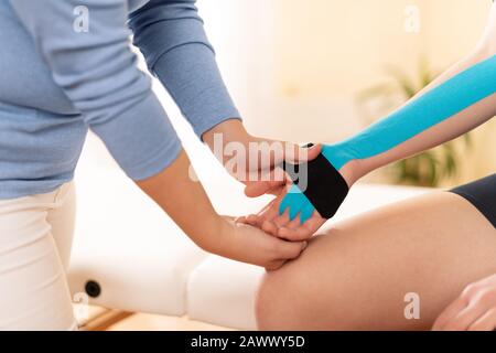 Female physiotherapist applying kinesio tape on patient's arm. Kinesiology, physical therapy, rehabilitation concept. Cropped shot side view. Stock Photo