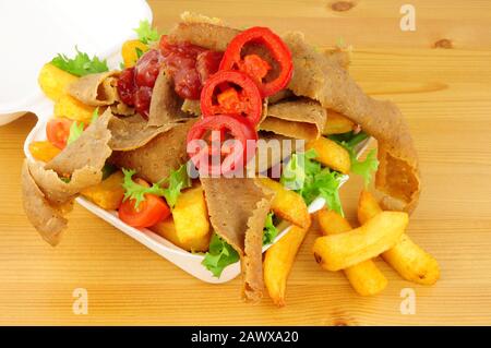 Doner kebab meat and chips with salad and chilli sauce in a take away tray on a wood background Stock Photo