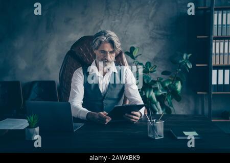 Concentrated pensive strict old man grandfather company owner sit table chair have job interview read attentive applicants candidates resume wear Stock Photo