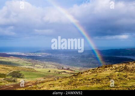 Rainbow on Tal y Fan mountain during changeable weather before storm Ciara in Snowdonia with view to Llandudno on coast. Conwy north Wales UK Britain Stock Photo