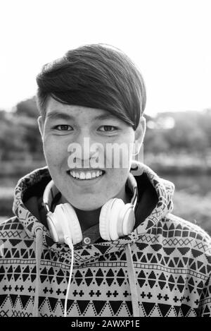 Young Asian teenage boy wearing headphones while relaxing at the park Stock Photo