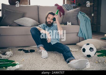 Portrait of his he nice attractive sick disappointed bearded guy sitting on floor suffering from pain early morning next day after party at industrial Stock Photo