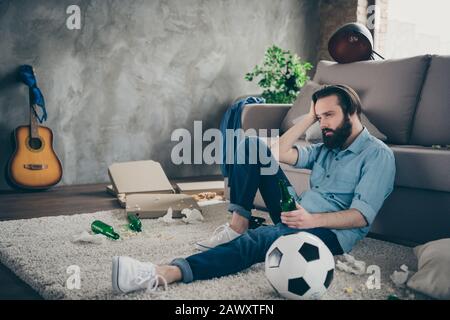 Portrait of his he nice attractive sad disappointed brunet guy sitting on floor suffering from hangover early morning at industrial loft modern style Stock Photo