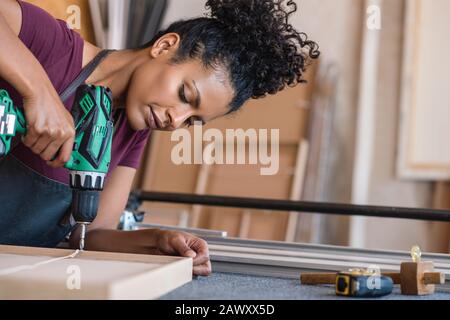 Woman assembling a frame using a drill in her workshop Stock Photo