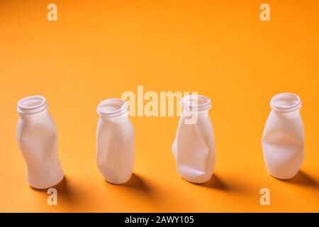 Four white disposable plastic bottles on orange background, conceptual studio horizontal shot Stock Photo