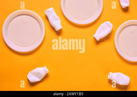 Horizontal flat lay composition of white plastic empty plates and bottles on orange background, copy space Stock Photo