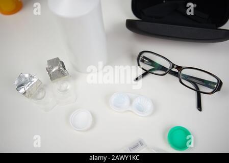 Multiple eye care products sitting on white counter top. Lenses in case with packaging, glasses, and more Stock Photo