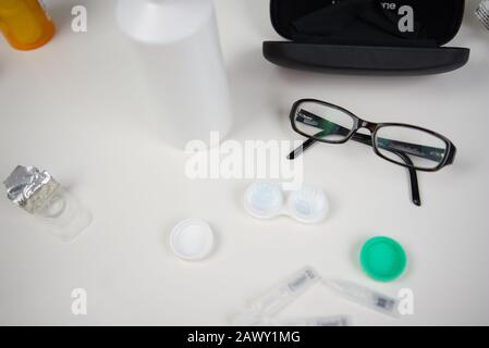 Contact lens case with glasses, case, frames, and drops in flat lay on white background of counter top Stock Photo