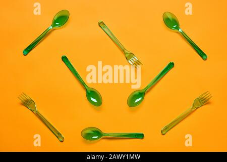 Horizontal flat lay conceptual shot of green plastic spoons and forks on bright orange background Stock Photo